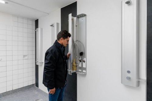 Schell_Vertriebsbeauftragter_Benjamin_Buschhaus_vor_einem_geo__ffneten_Duschpaneel_LINUS_DP-C-T_in_den_Duschra__umen_des_Schulzentrum_Nord