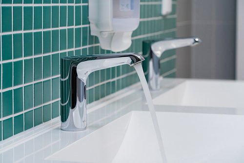 Close-up einer elektronischen Waschtisch-Armatur XERIS E HD-K in den Sanitärräumen der Gemeinschaftsgrundschule Theodor-Heuss in Wesel-Bislich mit laufendem Wasser.