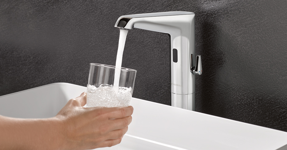 Wasser aus elektronischer Armatur füllt Trinkglas